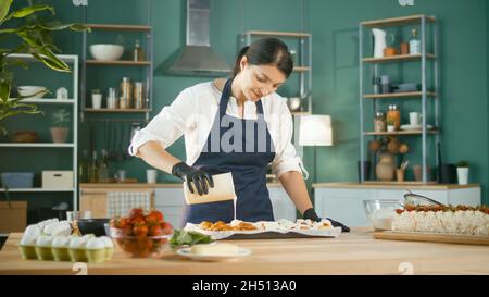 Ein zufriedener Konditormeister gießt das Sahnehäubchen auf frisch gebackene Zimtbrötchen oder Zimtbrötchen Stockfoto