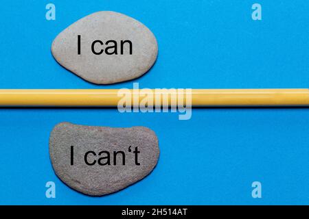 Die Worte, die ich kann und die ich nicht kann, sind auf natürlichen glatten Steinen geschrieben, die durch einen gelben Bleistift getrennt sind. Der Hintergrund ist blau isoliert und hat eine Menge SP Stockfoto