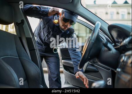 Polizeibeamter mit einer Taschenlampe, die das Auto überprüft Stockfoto