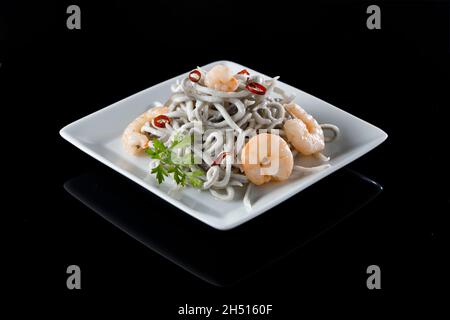 Portion Glutonie mit Garnelen und Chilischoten auf glänzend schwarzer Oberfläche Stockfoto