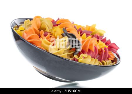 Ungekochte, farbige Fusilli-Pasta mit Keramikgeschirr, Nahaufnahme, isoliert auf Weiß. Stockfoto