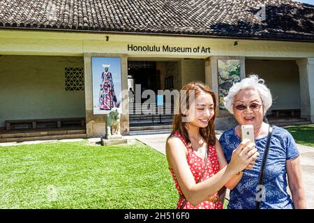 Honolulu Hawaii, Oahu, Hawaiian, Kunstmuseum, asiatisches Teenager-Mädchen älterer Bürger weibliche Großmutter, die nach dem Eingang zum iPhone schaut Stockfoto