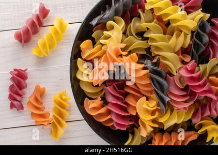 Ungekochte, farbige Fusilli-Pasta in einer Keramikschale auf einem Holztisch, Nahaufnahme, Draufsicht. Stockfoto