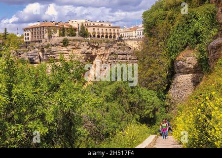 Ronda von der Schlucht Tajo aus gesehen. Die Wanderer steigen vom Weg, der zum Grund der Schlucht führt. Das Gebäude ist Ronda´s National para Stockfoto