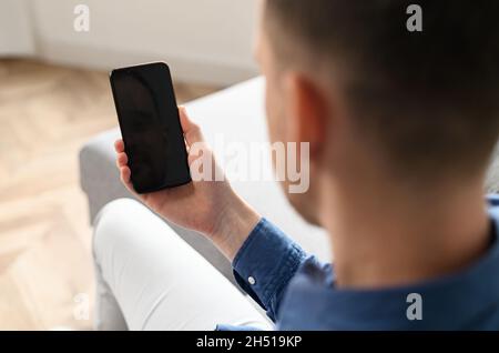 Rückansicht über die Schulter des jungen Mannes auf dem Smartphone mit leerem Bildschirm in den Händen, Modell Konzept. Ein Mann, der eine App verwendet und auf einem leeren mobilen Display zusieht. Platz kopieren, Werbekonzept Stockfoto