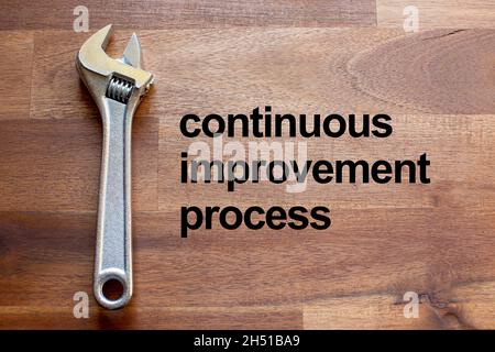 Auf einem dunklen Holztisch liegt ein flexibler verchromter verstellbarer Schraubenschlüssel. Der Solgan Continuous Improvement Process ist in schwarzen Buchstaben auf den Tisch geschrieben Stockfoto