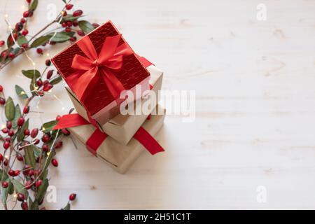 Drei Weihnachtsgeschenke gestapelt als Bordüre mit roten Beeren und Lichter mit roten Schleifen von oben auf weißem Hintergrund mit Kopierraum Stockfoto