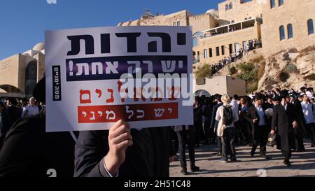 Ein Haredi-Jude hält ein Schild mit der Aufschrift „Judentum ist nur einer, Linke sind viele“, während sich Ultra-orthodoxe Juden während eines Protestes gegen „Frauen der Mauer“ versammeln. Beim Betreten des platzes der Westmauer mit Tora-Rollen in einer langjährigen Kampagne für die Gleichstellung der Geschlechter an dem Ort, der dem jüdischen Volk am 05. November 2021 in Jerusalem, Israel, geweiht ist. The Women of the Wall ist eine feministische Gebetsgruppe, die eine monatliche Gebetsstunde an der Western Wall veranstaltet und immer wieder behauptet hat, dass es keinen einzigen „Brauch des Ortes“ gibt und dass ihr Recht zu beten eine im ISR verankerte Religionsfreiheit ist Stockfoto