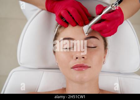 Kosmetologe macht Hardware Reinigung des Gesichts von schönen jungen Patienten. Konzept Hautreinigung und Wiederherstellung der Elastizität Stockfoto