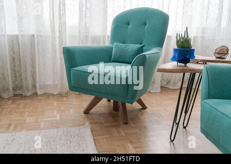 Türkisblaue Sessel am Fenster auf Parkettboden im Wohnzimmer Stockfoto