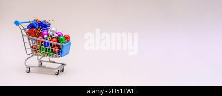 Konzept für die Weihnachtszeit Shopping Mini-Store-Warenkorb voller Geschenkboxen und Dekorationen, um den weihnachtsbaum zu schmücken, kleine bunte Kugeln auf einem hellrosa Hintergrund. Selektiver Fokus Stockfoto