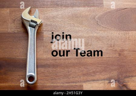 Auf einem dunklen Holztisch liegt ein flexibler verchromter verstellbarer Schraubenschlüssel. Der Solgan Join our Team ist in schwarzen Buchstaben auf dem Tisch geschrieben Stockfoto