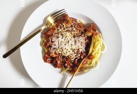 Spaghetti in einer weißen Schüssel mit einer Sauce aus San Marzano Tomaten, Pilzen und Speck. Goldene Gabel und Löffel. Stockfoto