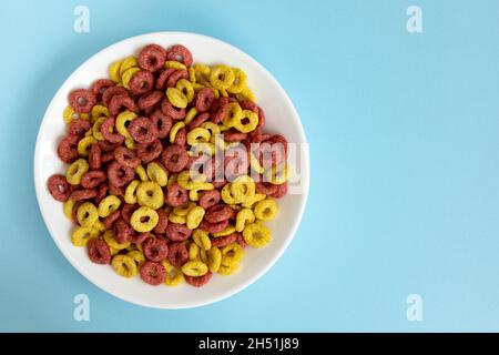 Schale aus Vollkorn-Getreideringen isoliert auf blauem Hintergrund, gesundes Frühstückskonzept, Platte mit köstlichen Ringen mit Ampty Platz für Text Stockfoto