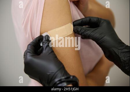 Nahaufnahme der Hände einer Krankenschwester in schützenden medizinischen Handschuhen, die ein Pfandband auf die Hände einer Frau legen, die gegen einen Coronavirus-Virus-Infekt geimpft wird Stockfoto