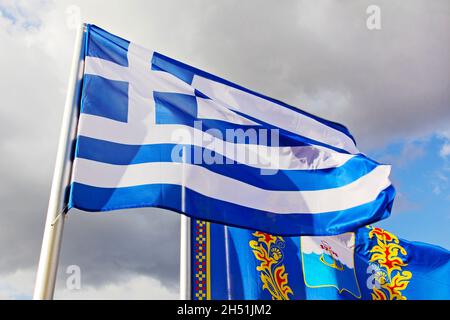 Griechische Flagge und Mariupol-Stadtflagge auf bewölktem Himmel beim griechischen Folklorefestival in Mariupol, Ukraine. Stockfoto