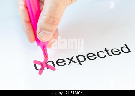 Das Präfix 'un' des Wortes Unexpected wird von einer Hand mit einem rosa Bleistift durchgestrichen Stockfoto