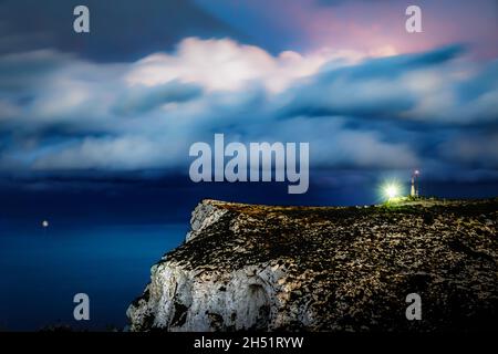 Der Abendhimmel hinter dem hellen Leuchtturm auf der Klippe über dem Meer. Stockfoto