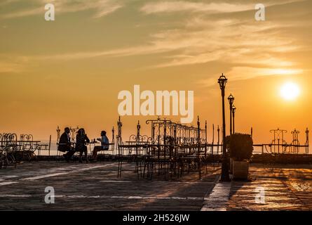 Saranda, Albanien - September 2016: Restaurant im Schloss Lekursi in Saranda, Albanien. Ionisches Meer, Sonnenuntergang. Silhouette? Von Menschen, die am Tisch sitzen Stockfoto