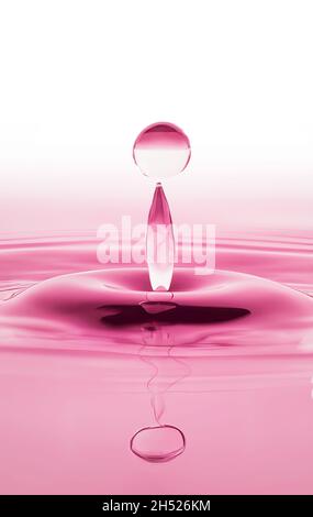 Tropfen, der in rosa Tönen auf die Wasseroberfläche fällt Stockfoto