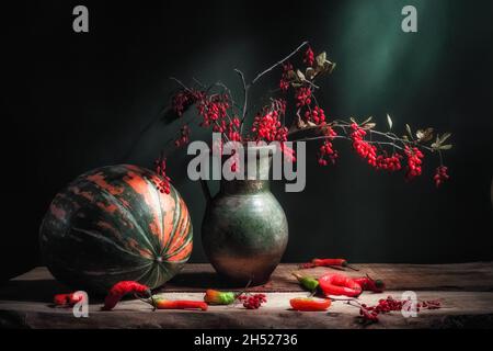 Klassisches Stillleben mit großen gestreiften Pampkin, schöner Berberis-Berberberbeerzweig mit roten Beeren im alten Vintage-Krug und heißer roter Paprkia auf Holz Stockfoto