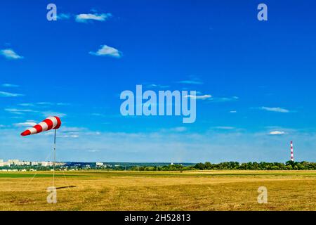 Rot-weiße Windsocke auf blauem Himmel, grünes Feld und Wolken Hintergrund auf Flugplatz oder Flugplatz. Zeigt windgeschwindigkeit und -Richtung an. Stockfoto