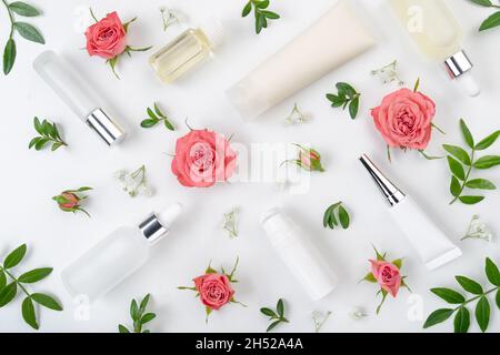 Flache Kosmetikflaschen und -Behälter mit rosa Rosen und grünem Blatthintergrund auf weißem Tisch Stockfoto