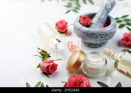 Handgemachte Rosenkosmetik-Konzept aus Mörtel und Stößel mit Rosenknospen mit Tropf und Flaschen mit Serum und Öl auf weißem Hintergrund Stockfoto