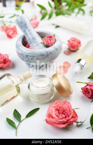 Handgemachte Rosenkosmetik-Konzept aus Mörtel und Stößel mit Rosenknospen mit Tropf und Flaschen mit Serum und Öl auf weißem Hintergrund Stockfoto