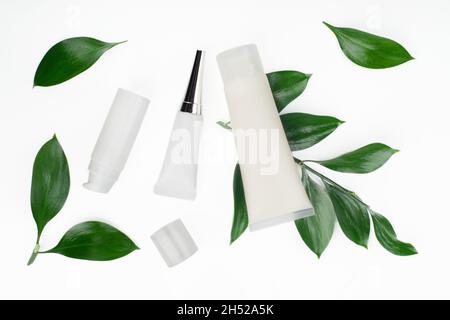 Flache Sicht auf weiße Kosmetikflaschen und Behälter mit grünen Blättern auf weißem Tisch Stockfoto
