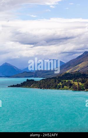 Grüne Kaps und schneebedeckte Berge am Ufer des Lake Wakatipu. Südinsel, Neuseeland Stockfoto