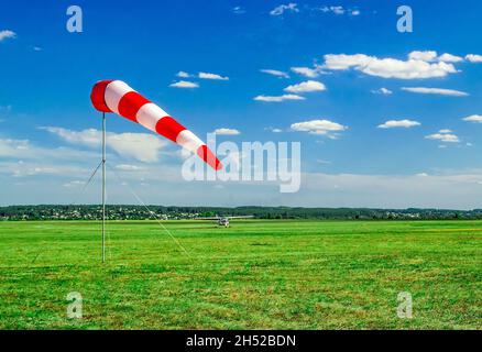 Rot-weiße Windsocke auf blauem Himmel, grünes Feld und Wolken Hintergrund auf Flugplatz oder Flugplatz. Zeigt windgeschwindigkeit und -Richtung an. Stockfoto