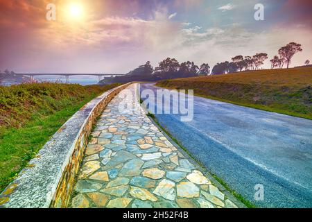 Promenade Lighthouse Road (Estrada do faro) entlang der Bucht Ria de Ribadeo del EO. Puente de Los Santos Brücke im Hintergrund. Ribadeo, Spanien Stockfoto