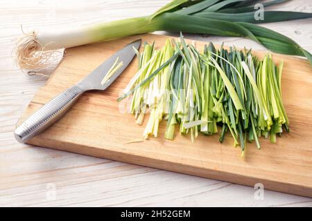 Frischer Lauch in dünne Streifen geschnitten und ein Küchenmesser auf einem Holzbrett, zubereitetes Gemüse für das Kochen eines gesunden vegetarischen Gerichts, Kopierer Platz, selecte Stockfoto