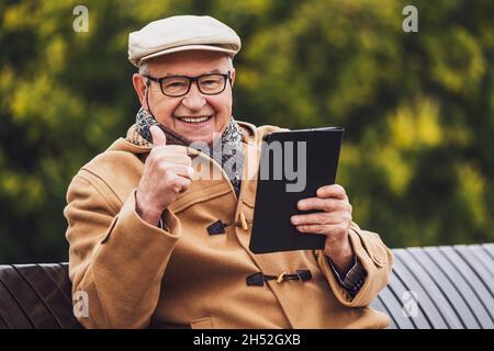 Porträt eines fröhlichen älteren Mannes im Wintermantel, der ein digitales Tablet verwendet. Stockfoto