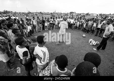 JOHANNESBURG, SÜDAFRIKA - 12. Aug 2021: Eine Graustufenaufnahme eines freiwilligen Fußballtrainers, der mit afrikanischen Kindern auf einem Schulhof in Johann arbeitet Stockfoto