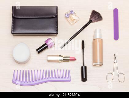 Grundinhalt der Kosmetiktasche auf hellem Holztisch, flach liegend. Essential Make-up Beauty-Produkte und Frauen Accessoires Stockfoto