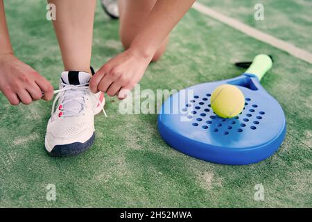 Die Athlet bindet die Spitze auf dem Padel Court, mit einem Schläger und Ball neben ihr. Hochwertige Fotos Stockfoto