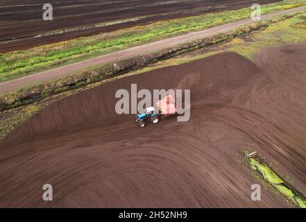 Torf-Harvester-Traktor zum Sammeln von entpackenden Torfböden. Bergbau und Ernte von Torfland. Die aus dem Schlamm entwässerten Flächen werden für die Torfgewinnung verwendet. Abfluss Stockfoto