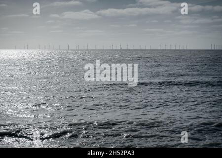 Offshore-Windenergieanlagen am Horizont in Clacton-on-Sea, Essex, mit grauem Meer im Vordergrund und graublauem Himmel im Hintergrund. Stockfoto