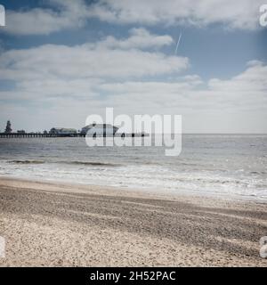 Clacton Pier (Clacton-on-Sea, Essex, UK) am Horizont; Meer und Strand im Vordergrund; blauer Himmel mit weißen Wolken und Flugzeugdampfpfad im Hintergrund. Stockfoto