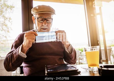 Älterer Mann sitzt im Café mit Gesichtsschutzmaske. Covid 19 Präventionskonzept. Stockfoto