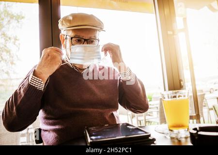 Älterer Mann sitzt im Café mit Gesichtsschutzmaske. Covid 19 Präventionskonzept. Stockfoto