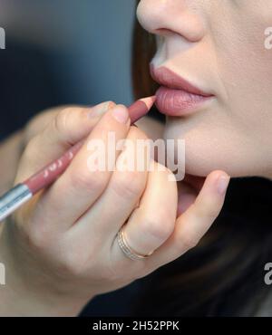 Make-up Artist Hand zeichnet Lippen Konturen auf einem Mädchen Gesicht mit Kosmetikstift. Schönheitssalon. Stockfoto