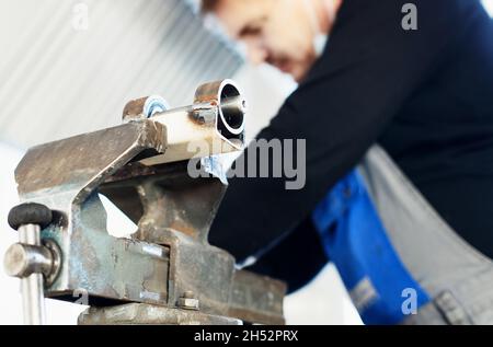 Ein Arbeiter in Overalls arbeitet hinter einer Werkbank mit Metallvisieren. Produktion von Metallteilen im Werk. Montage der Ausrüstung. Stockfoto