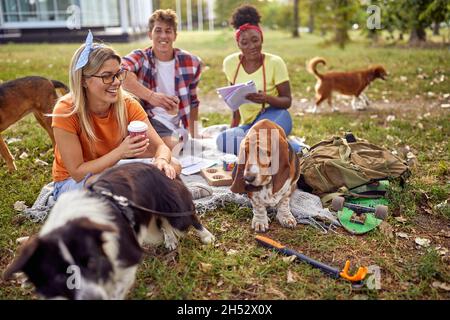 Gruppe von Studenten, die zusammen mit ihren Hunden ein Picknick machen Stockfoto