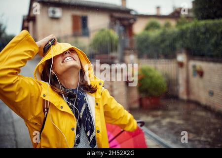 Ein junges Mädchen auf der Straße genießt Regen und hört in fröhlicher Atmosphäre der Musik zu. Spaziergang, Regen, Stadt Stockfoto