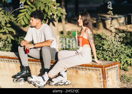 Zwei junge Freunde trinken alkoholfreie Getränke, während sie in Inline-Skates sitzen Stockfoto