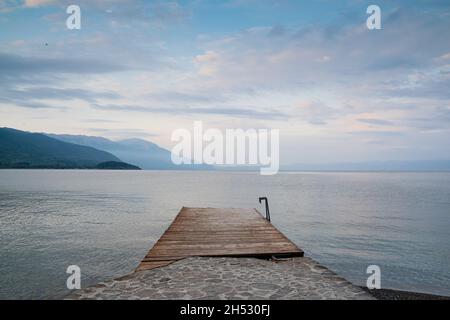 Vorderansicht Landschaft von leeren hölzernen Schwimmsteg Pier am See Ohrid mit schönen Küsten-Bergpanorama im Hintergrund Stockfoto