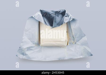 Draufsicht Nahaufnahme von geöffnetem frischem Butterstück in silberner Folienschutzverpackung auf grauem Hintergrund Stockfoto